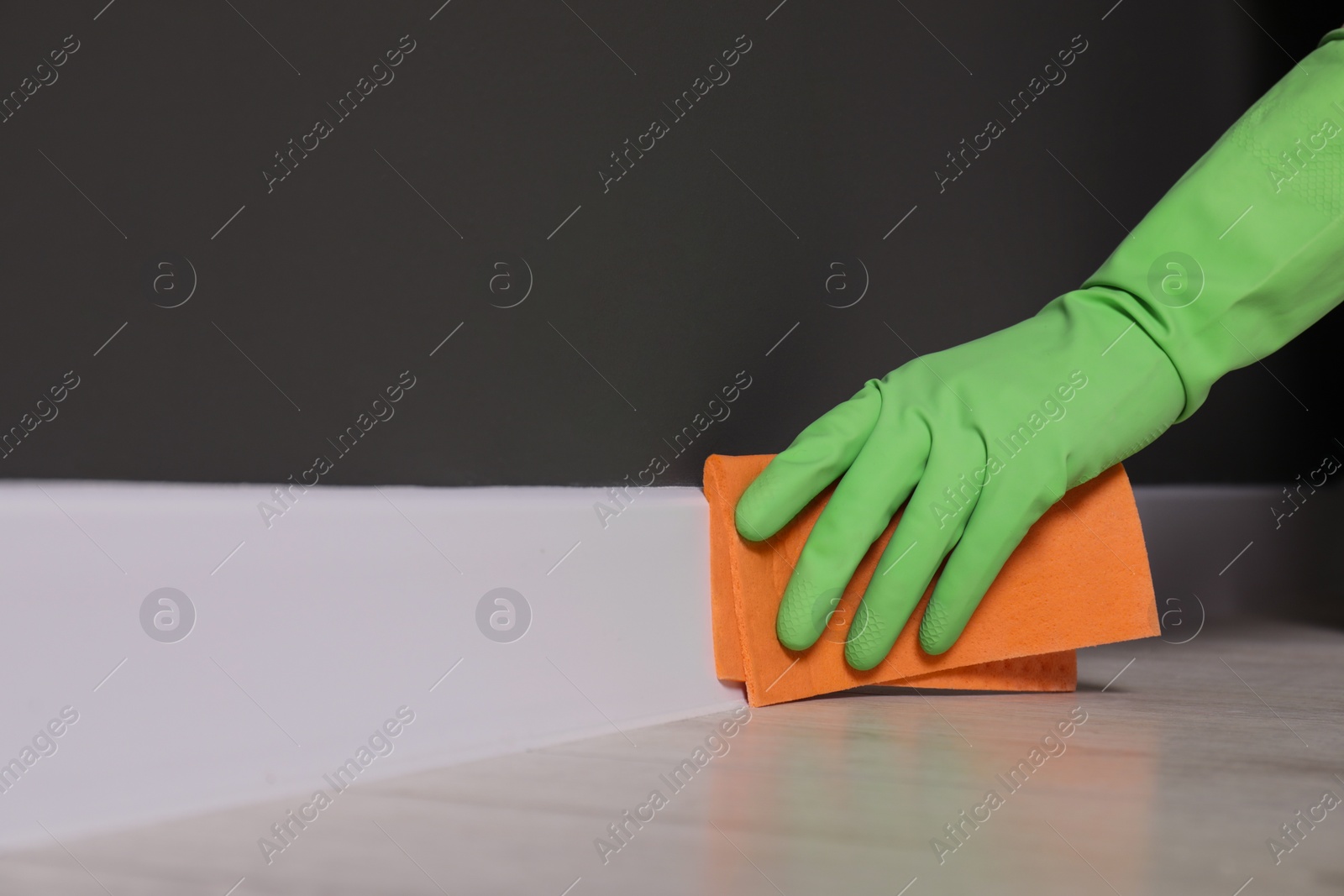 Photo of Woman in protective glove cleaning plinth with sponge cloth indoors, closeup. Space for text