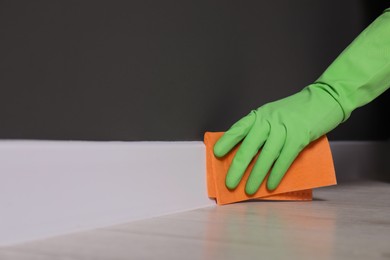 Photo of Woman in protective glove cleaning plinth with sponge cloth indoors, closeup. Space for text