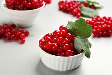 Photo of Delicious red currants and leaves in bowl on light table