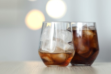 Photo of Glasses of cola with ice on table against blurred background