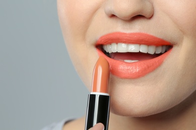 Young woman applying beautiful lipstick on gray background, closeup