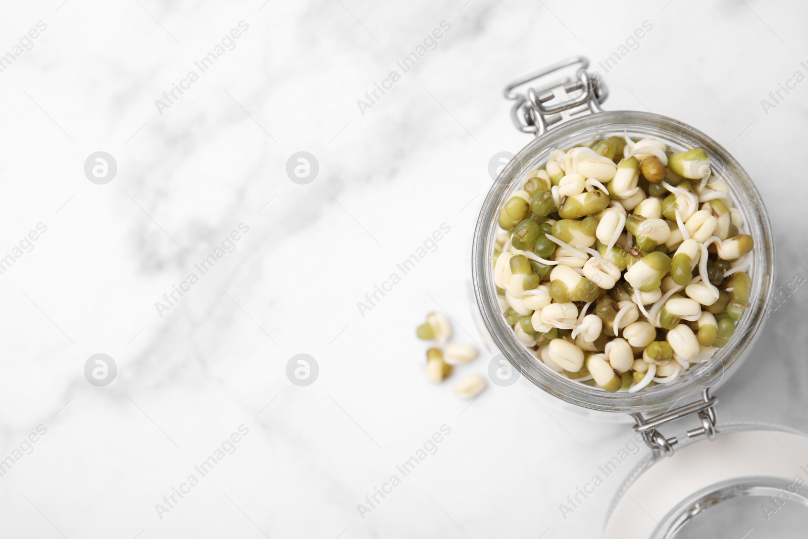 Photo of Glass jar with sprouted green mung beans on white marble table, top view. Space for text