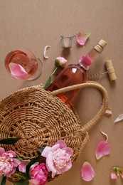 Photo of Flat lay composition with rose wine, wicker bag and beautiful pink peonies on brown background