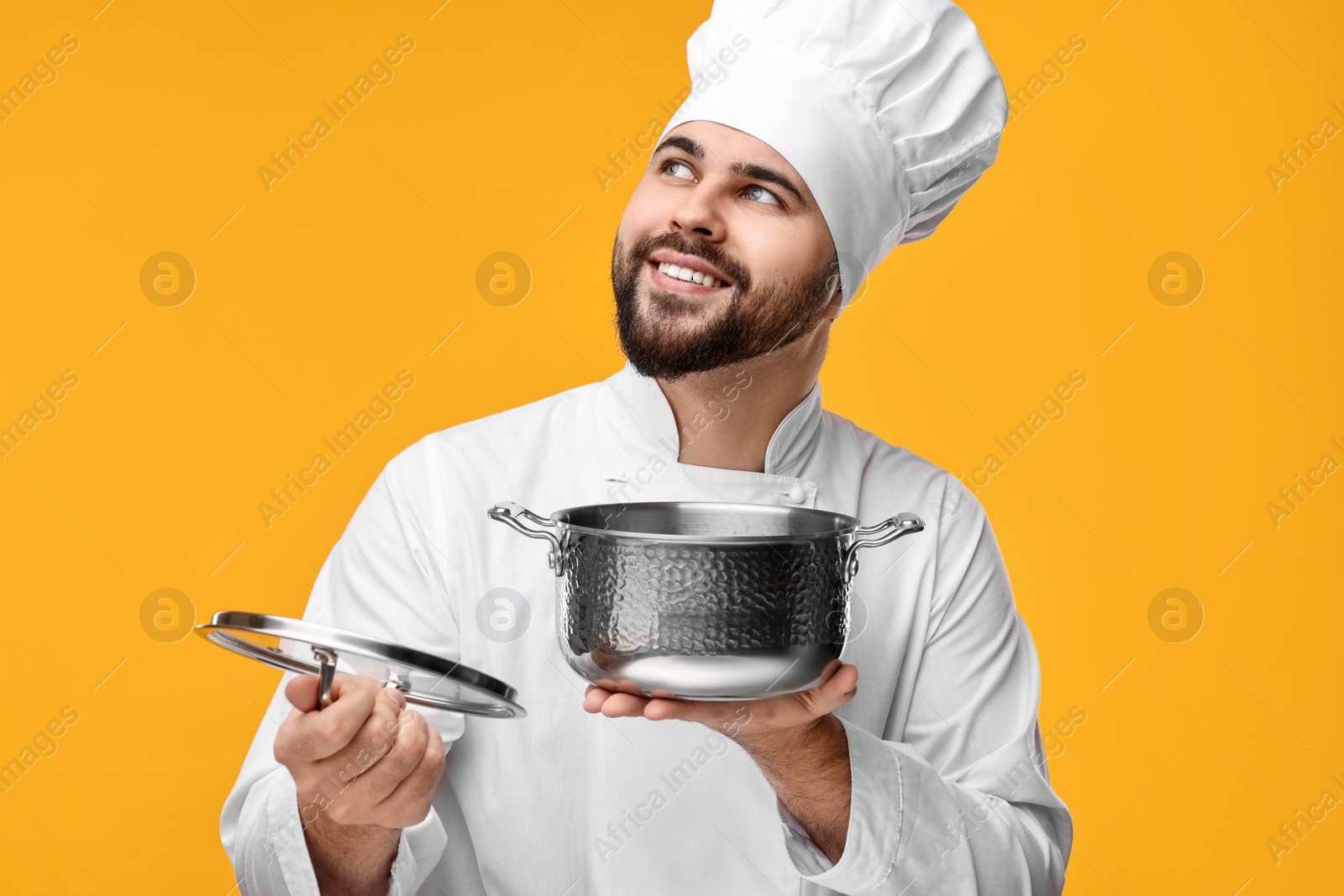 Photo of Happy young chef in uniform holding cooking pot on orange background