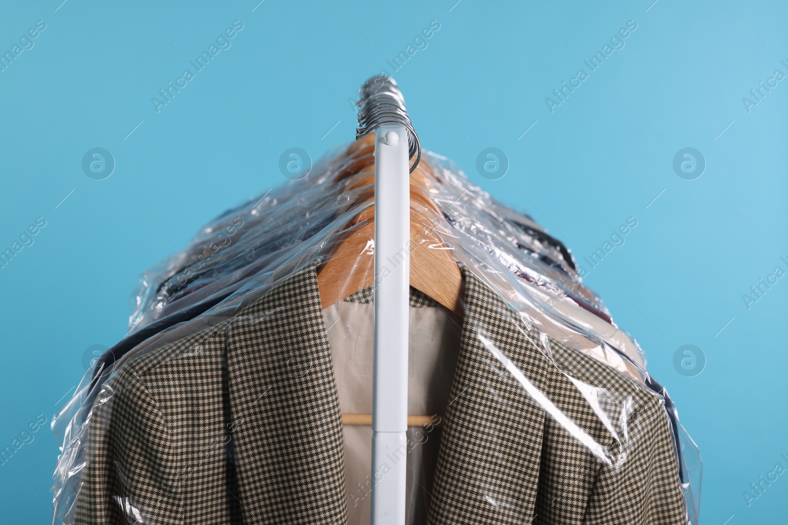 Photo of Dry-cleaning service. Many different clothes in plastic bags hanging on rack against light blue background