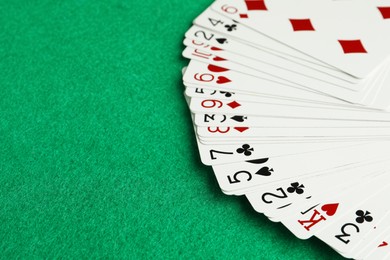 Photo of Fan of playing cards on green table, closeup. Space for text