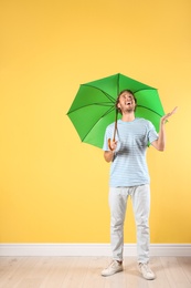 Man with green umbrella near color wall