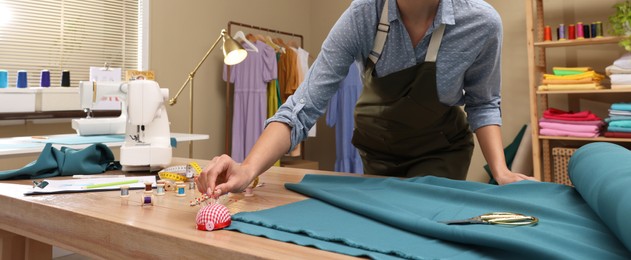 Dressmaker taking pin from cushion in workshop, closeup. Banner design