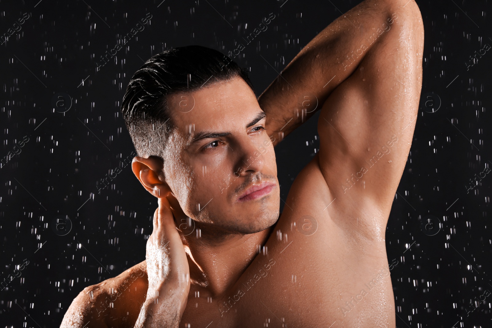 Photo of Man washing hair while taking shower on black background