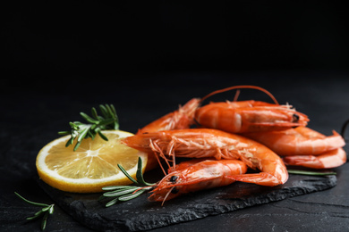 Delicious cooked shrimps with lemon and rosemary on black table