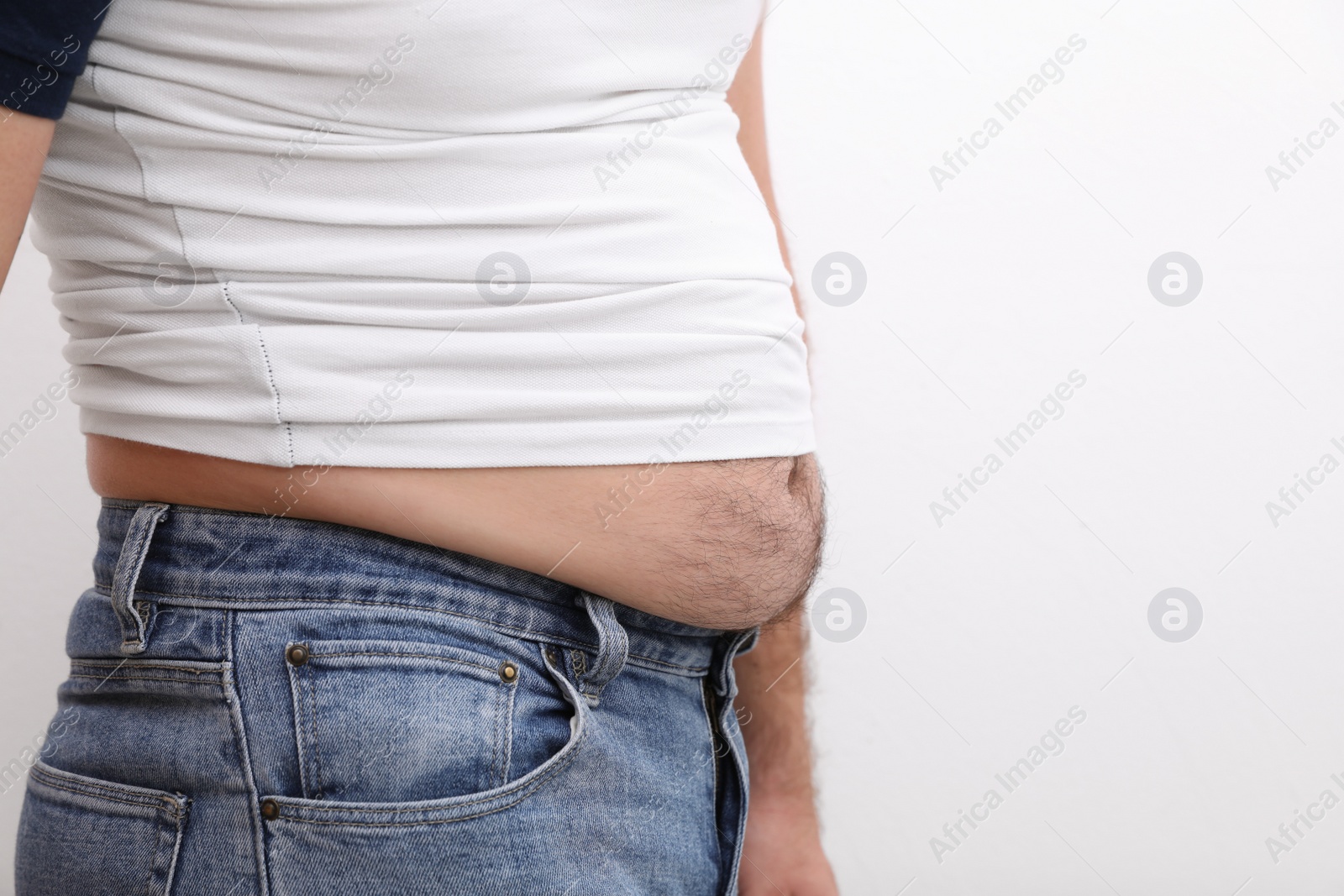 Photo of Man wearing tight t-shirt and jeans on white background, closeup. Overweight problem