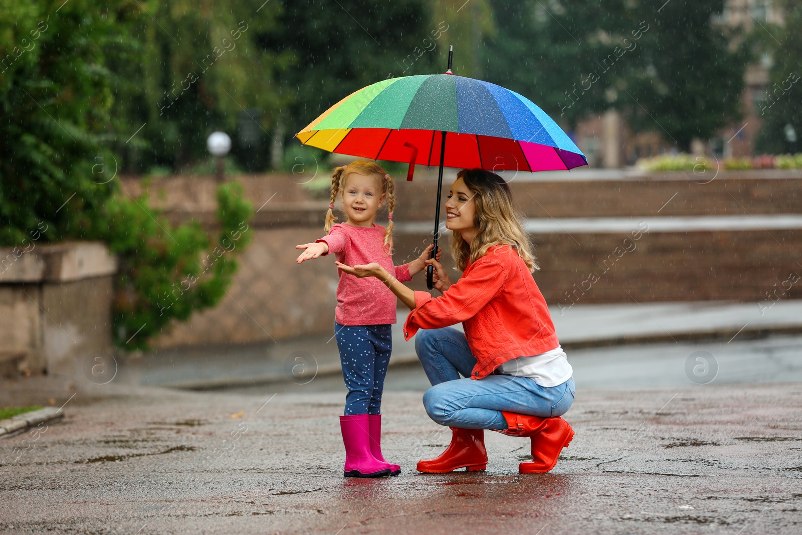 Photo of Happy mother and daughter with bright umbrella under rain outdoors