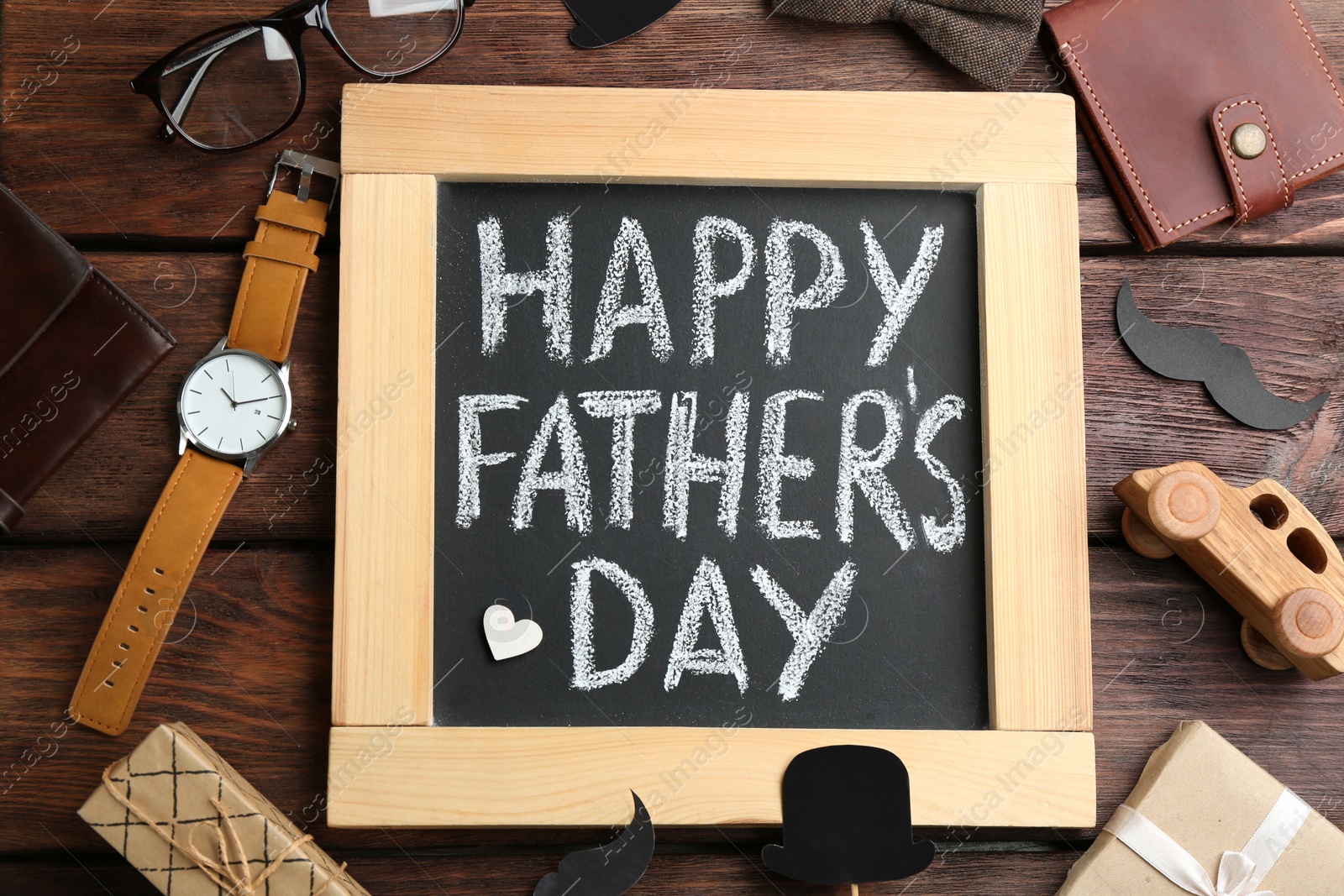 Photo of Blackboard with words HAPPY FATHER'S DAY and male accessories on wooden background, flat lay