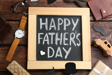 Photo of Blackboard with words HAPPY FATHER'S DAY and male accessories on wooden background, flat lay