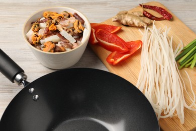 Photo of Black wok and products on light wooden table, closeup