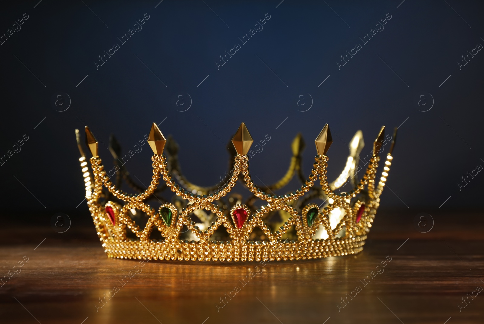 Photo of Beautiful golden crown with gems on wooden table. Fantasy item