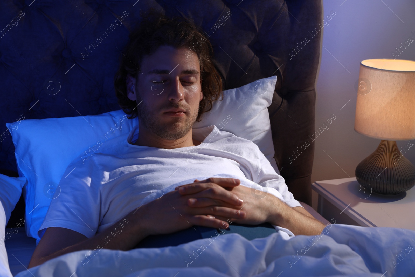 Photo of Handsome young man sleeping with book on pillow at night. Bedtime