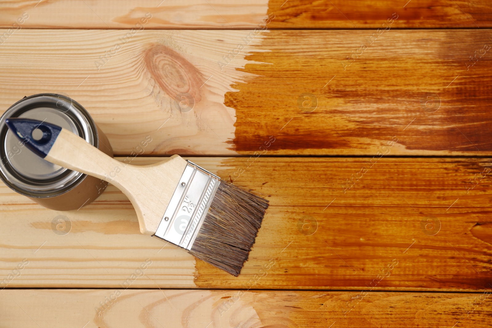 Photo of Brush and can with wood stain on wooden surface, top view. Space for text