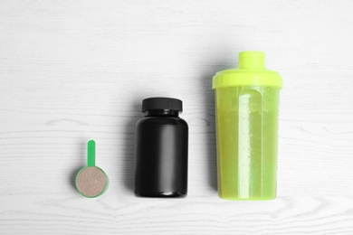 Bottle of protein shake, jar and scoop with powder on white wooden background, top view