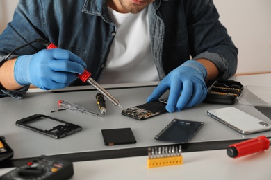 Technician repairing broken smartphone at table, closeup