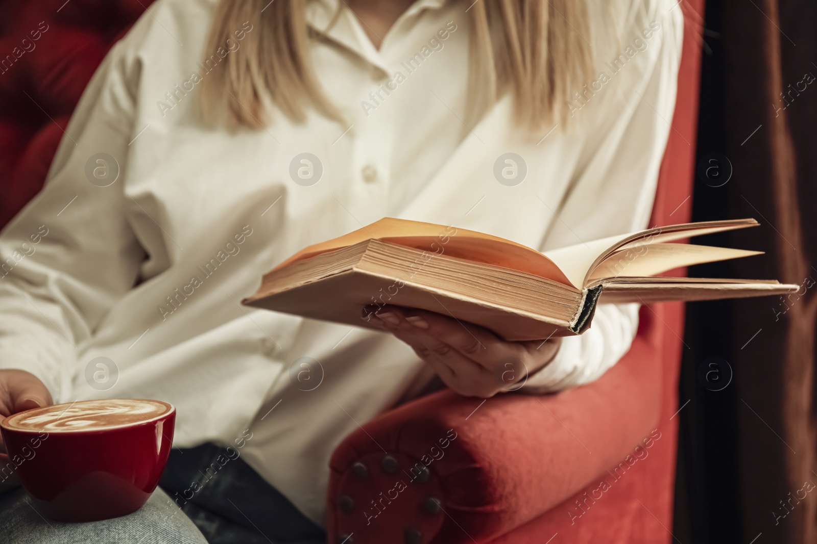 Photo of Woman with cup of coffee reading book indoors, closeup