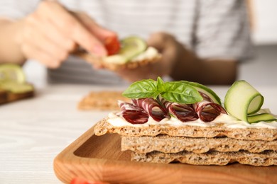 Fresh rye crispbreads with salami, cream cheese and cucumber on table, closeup