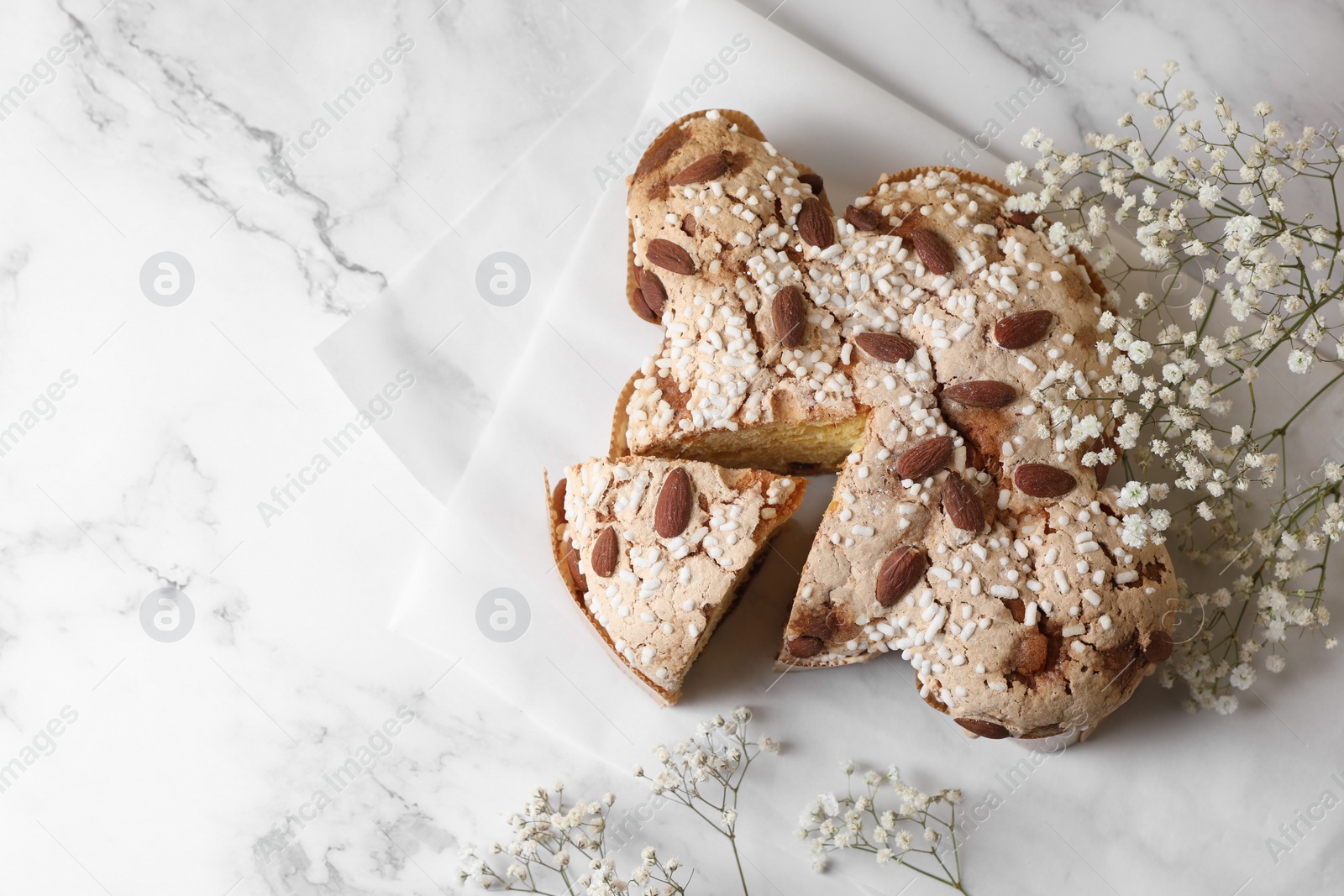 Photo of Delicious Italian Easter dove cake (traditional Colomba di Pasqua) and beautiful flowers on white marble table, top view. Space for text