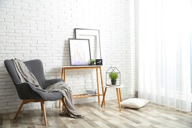 Stylish living room interior with comfortable armchair near brick wall. Space for text