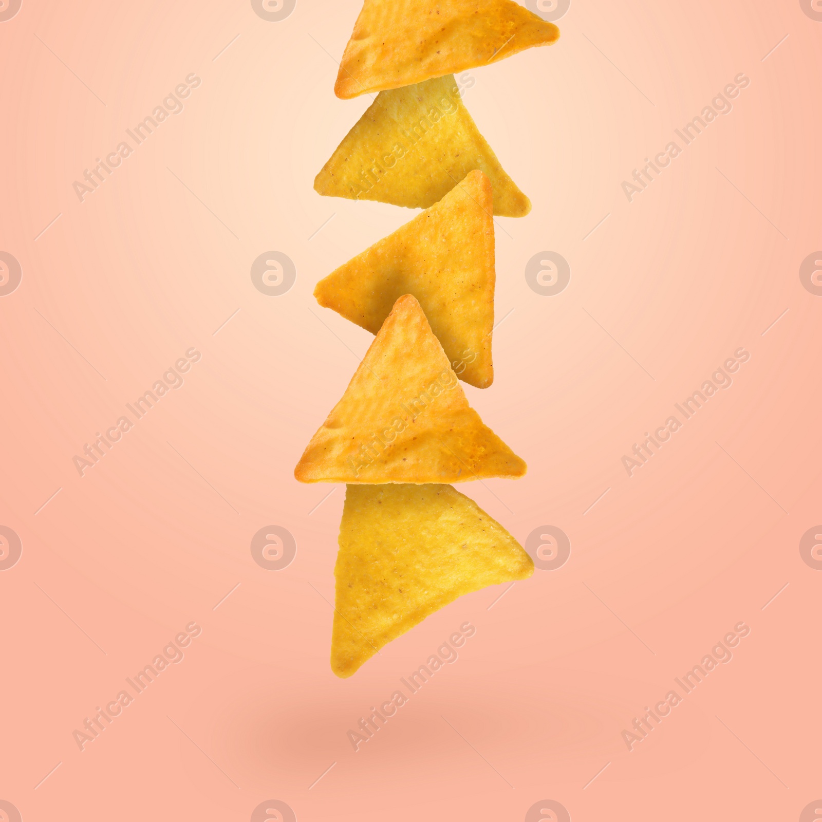 Image of Tasty tortilla chips falling on light coral background