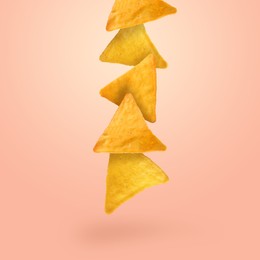 Tasty tortilla chips falling on light coral background