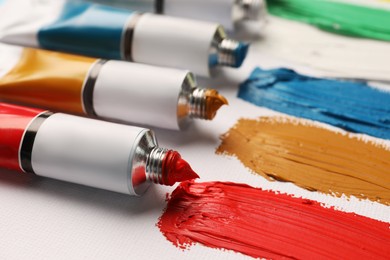 Photo of Tubes with oil paints and strokes on white canvas, closeup