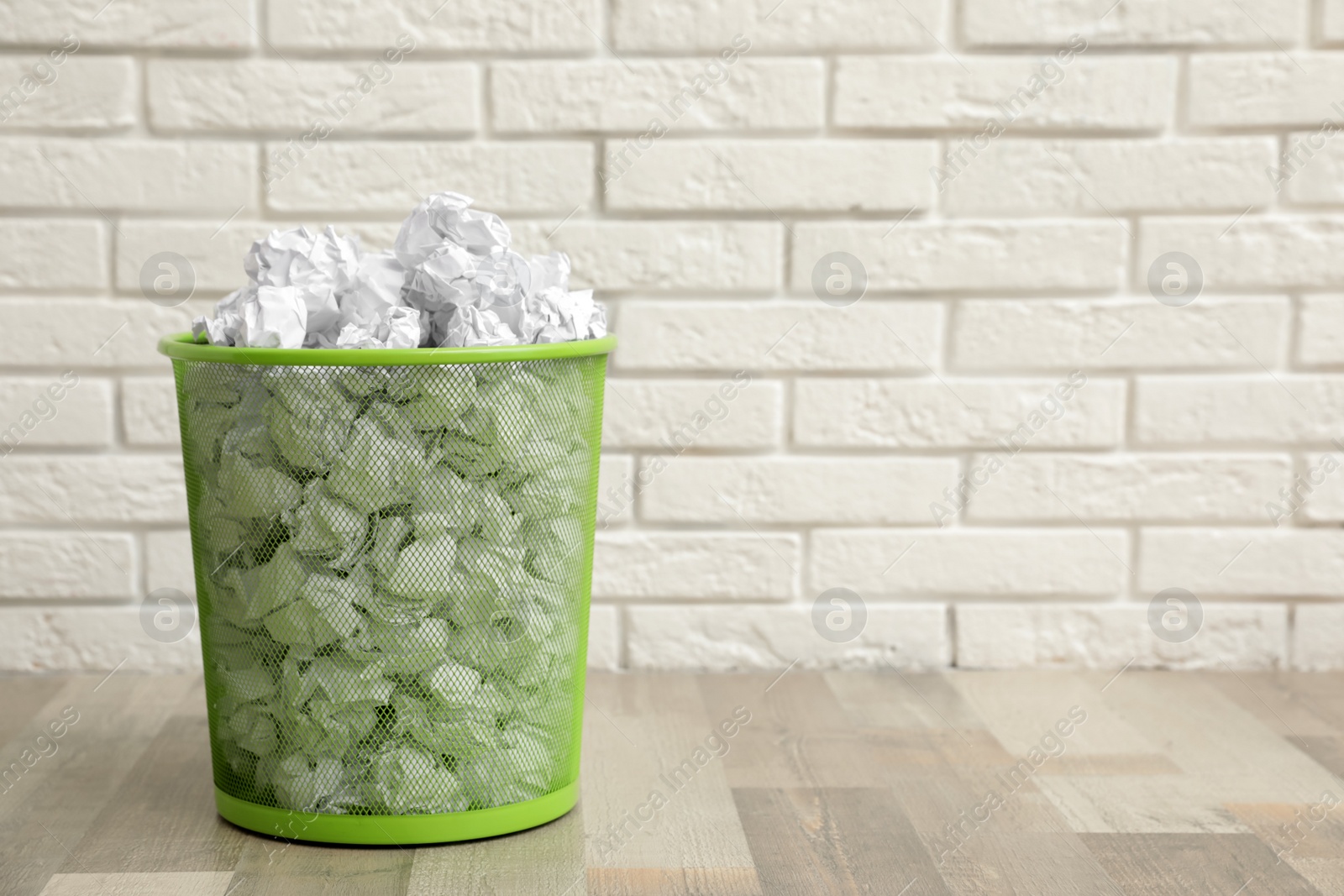 Photo of Metal bin with crumpled paper on floor against brick wall, space for text