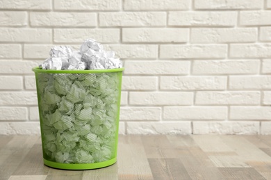 Photo of Metal bin with crumpled paper on floor against brick wall, space for text