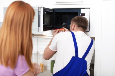 Housewife and repairman near microwave oven in kitchen