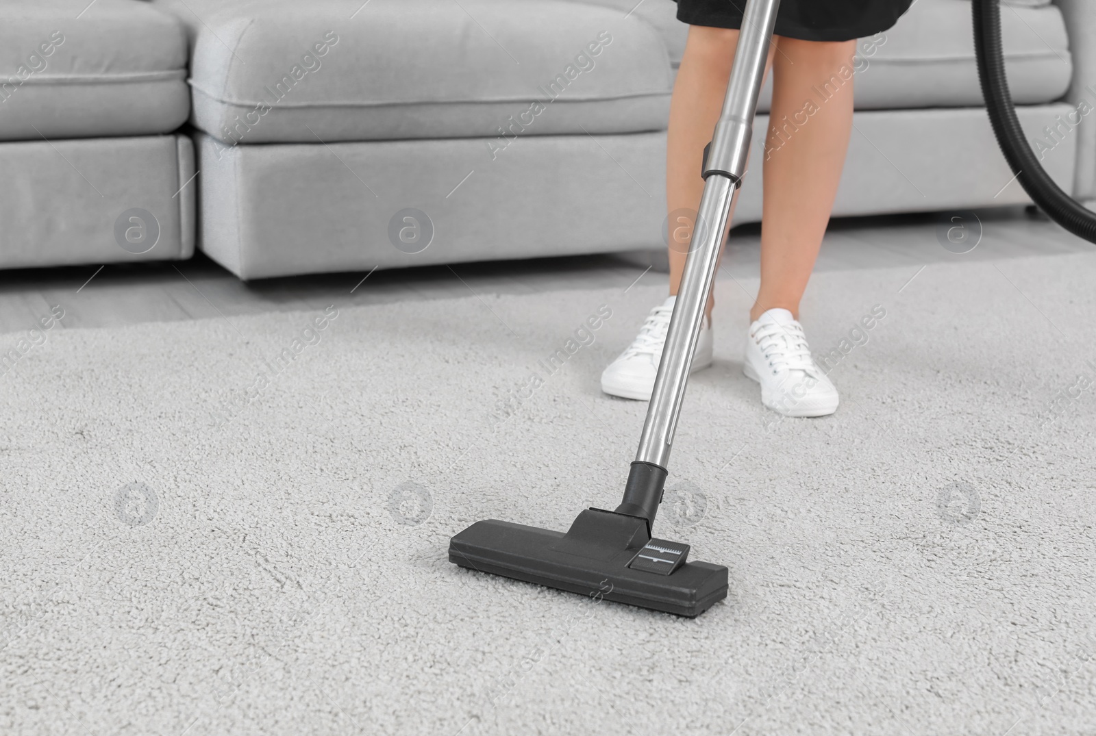 Photo of Female worker removing dirt from carpet with professional vacuum cleaner indoors