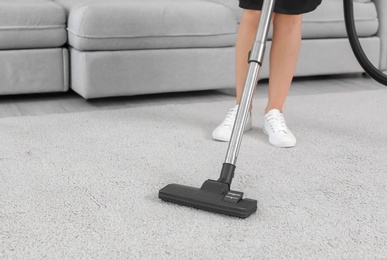 Photo of Female worker removing dirt from carpet with professional vacuum cleaner indoors