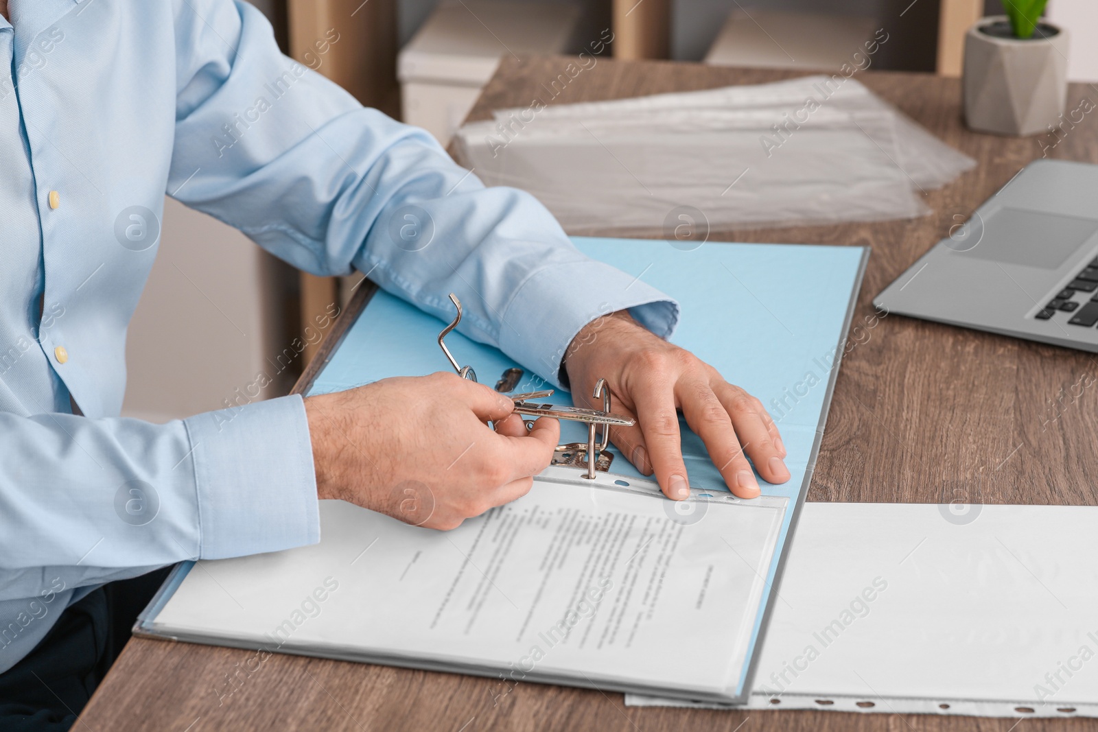 Photo of Businessman putting document into file folder at wooden table in office, closeup