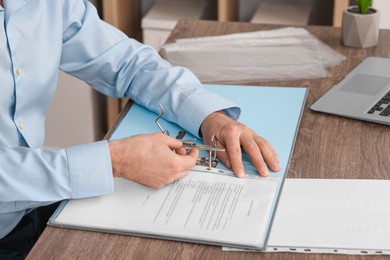 Photo of Businessman putting document into file folder at wooden table in office, closeup