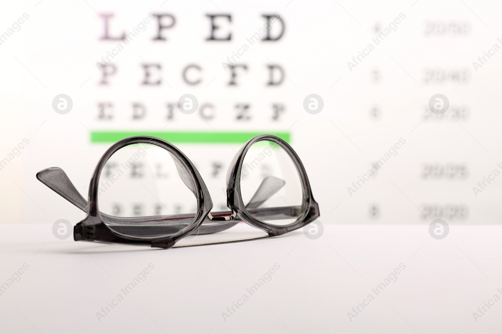 Glasses with corrective lenses on table against eye chart Photo of Glasses with corrective lenses on table against eye chart