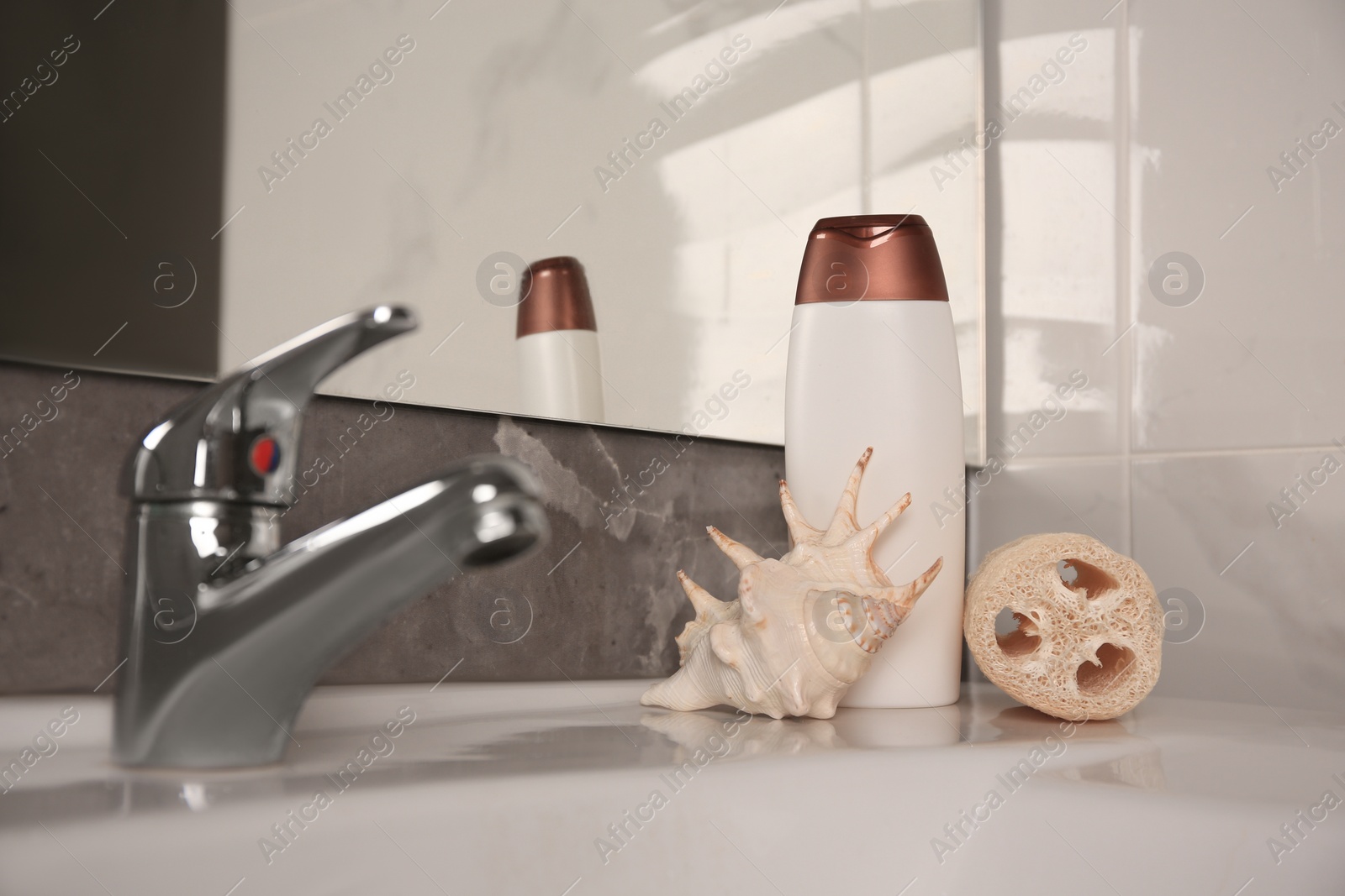 Photo of Natural loofah sponge, seashell and bottle of shower gel on washbasin in bathroom