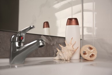 Photo of Natural loofah sponge, seashell and bottle of shower gel on washbasin in bathroom