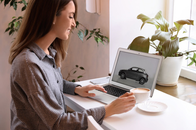 Photo of Woman using laptop to buy car at table indoors