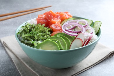 Delicious poke bowl with salmon, seaweed and vegetables served on light grey table