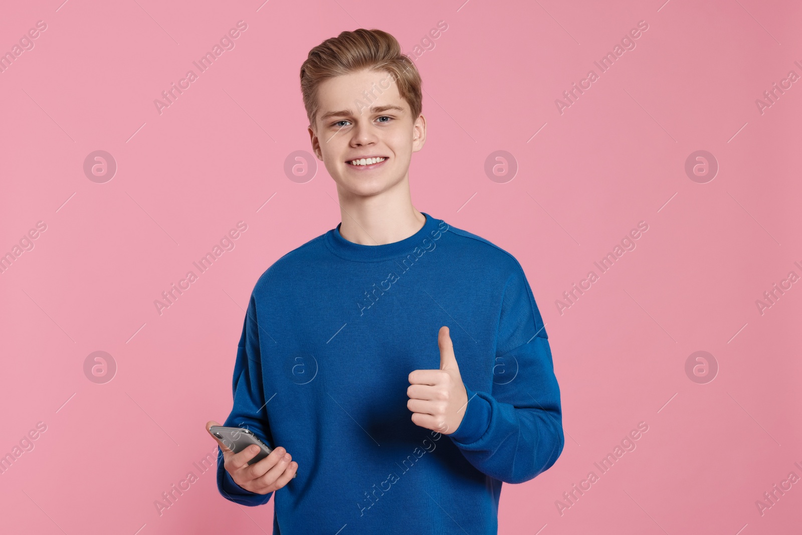 Photo of Teenage boy with smartphone showing thumb up on pink background
