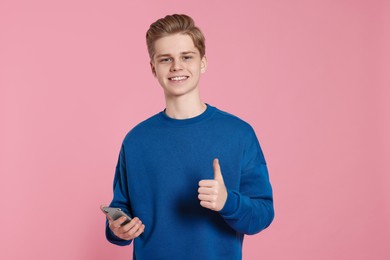 Teenage boy with smartphone showing thumb up on pink background