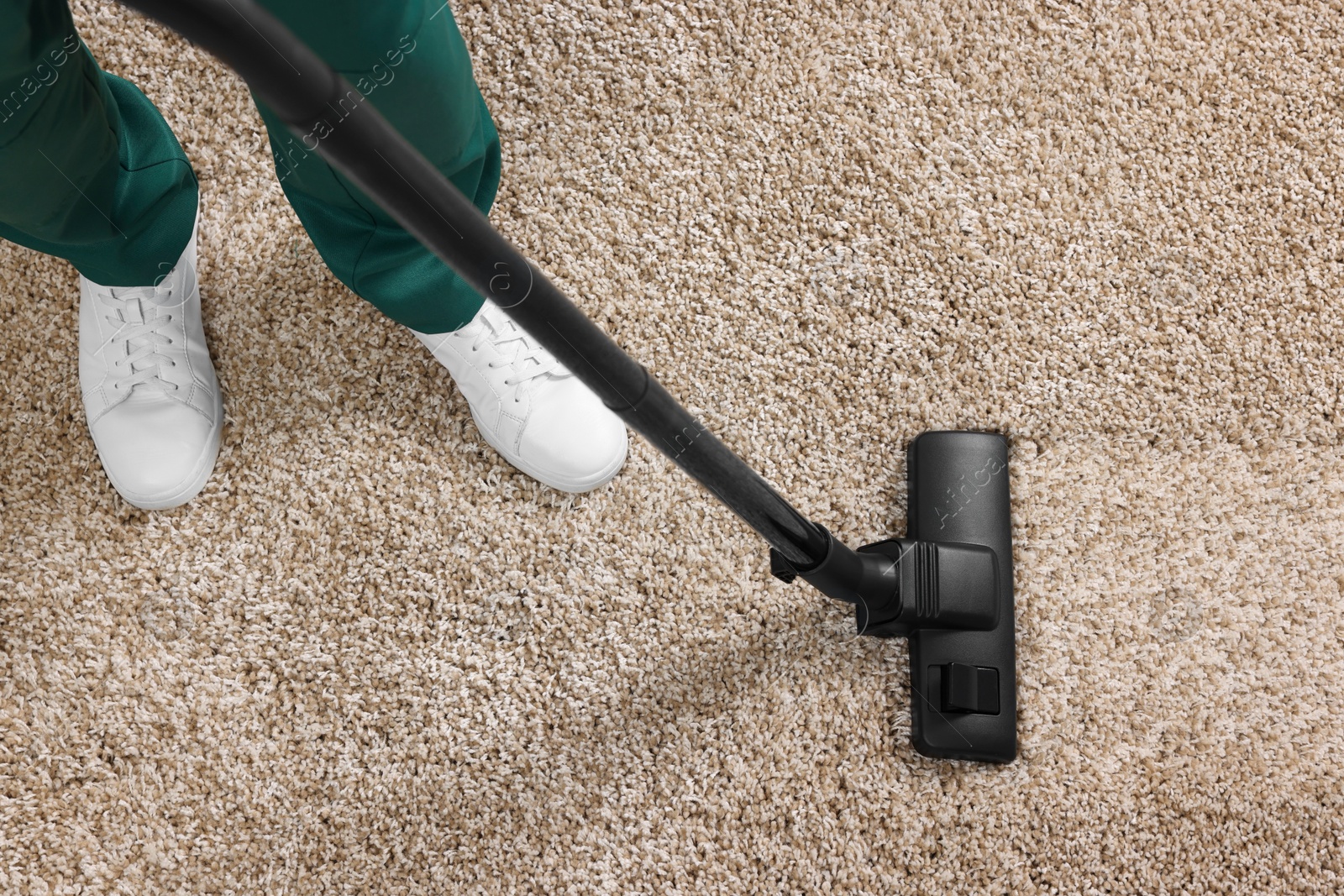 Photo of Dry cleaner's employee hoovering carpet with vacuum cleaner, above view