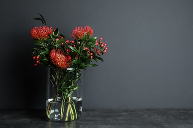 Bouquet with beautiful red protea flowers in glass vase on table against black background. Space for text