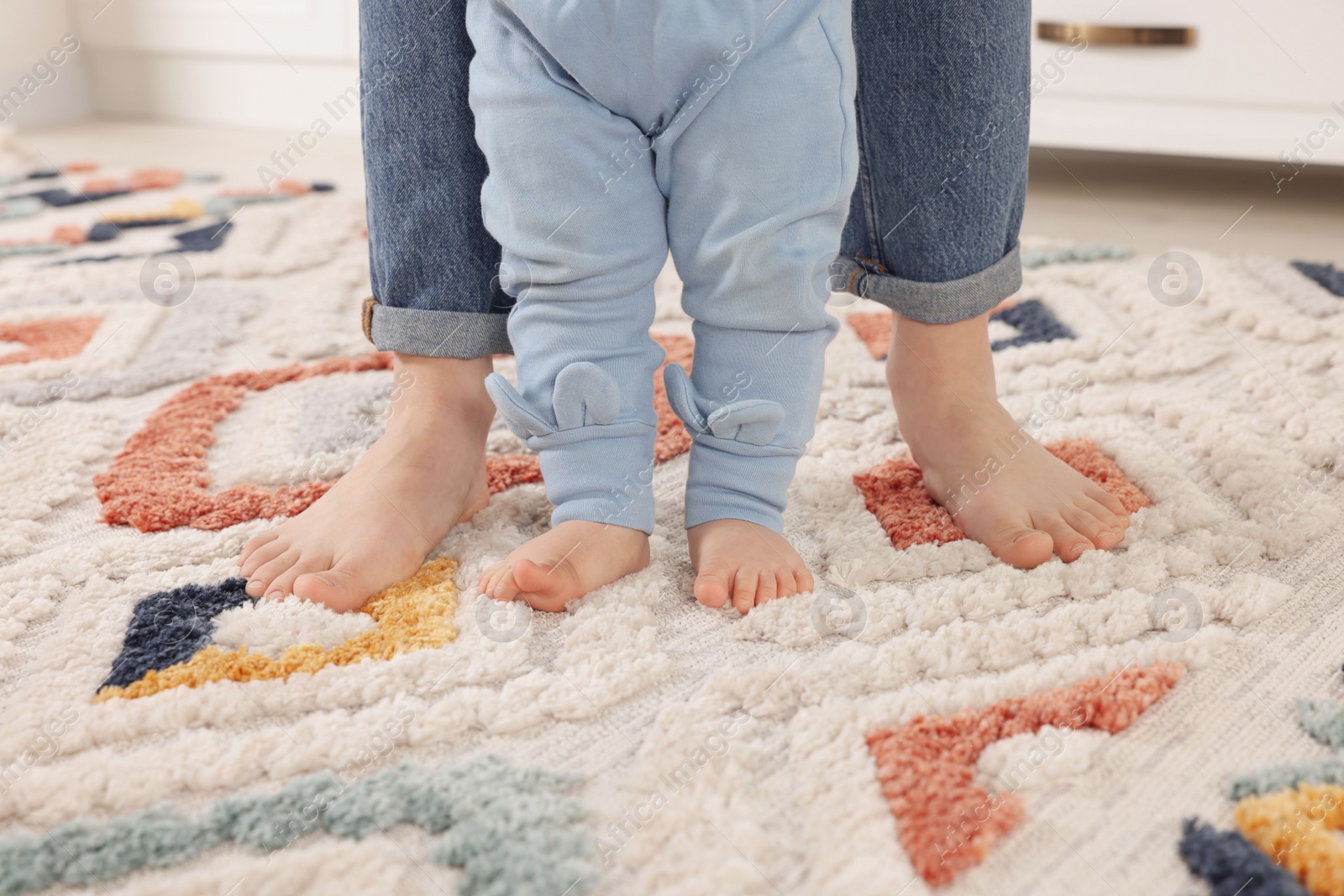 Photo of Mother supporting her baby son while he learning to walk on carpet indoors, closeup