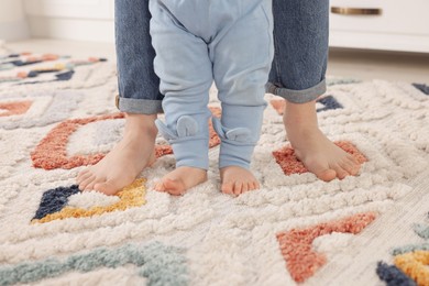 Photo of Mother supporting her baby son while he learning to walk on carpet indoors, closeup