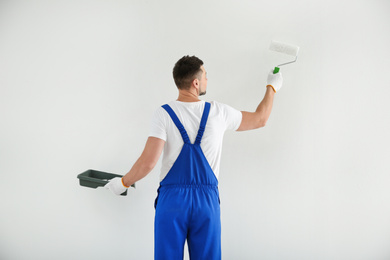 Photo of Man painting wall with white dye indoors, back view